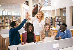 A diverse group of five people. Three of them smile at a laptop while the other two high-five behind them. 