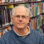 Board Member David Worth sitting in front of a bookshelf of books