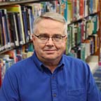 Board Member Gerald Wortman sitting in front of a bookshelf of books
