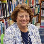 Board Member Nancy Wharmby sitting in front of a bookshelf of books