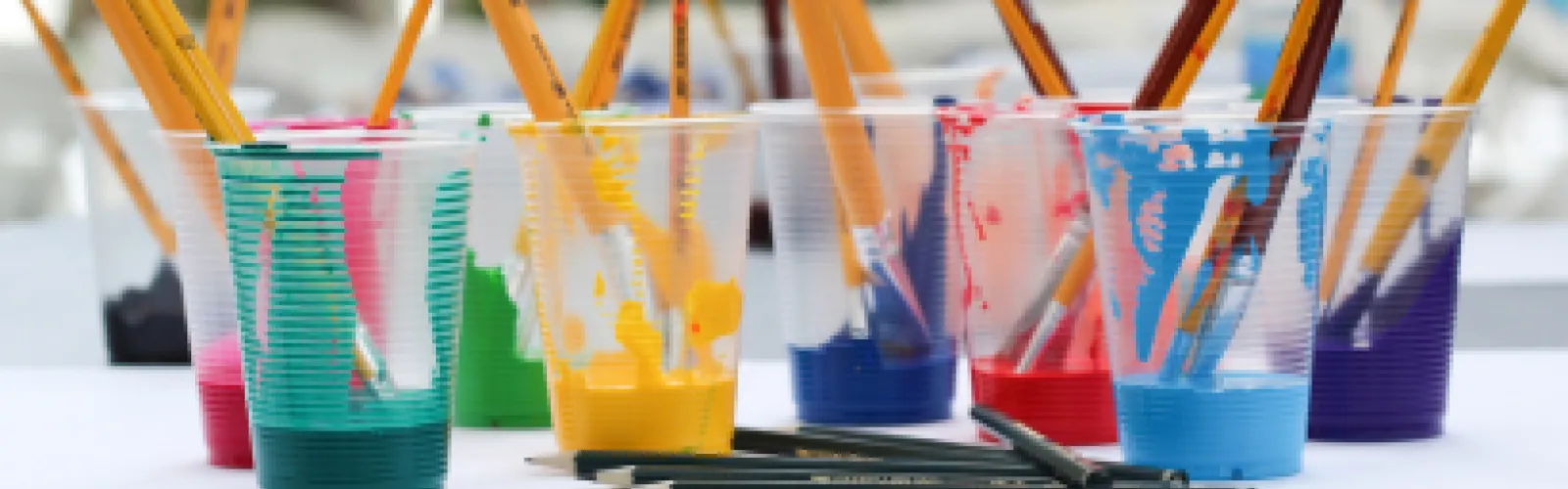 Several plastic cups of paint with paint brushes sticking out of them. 